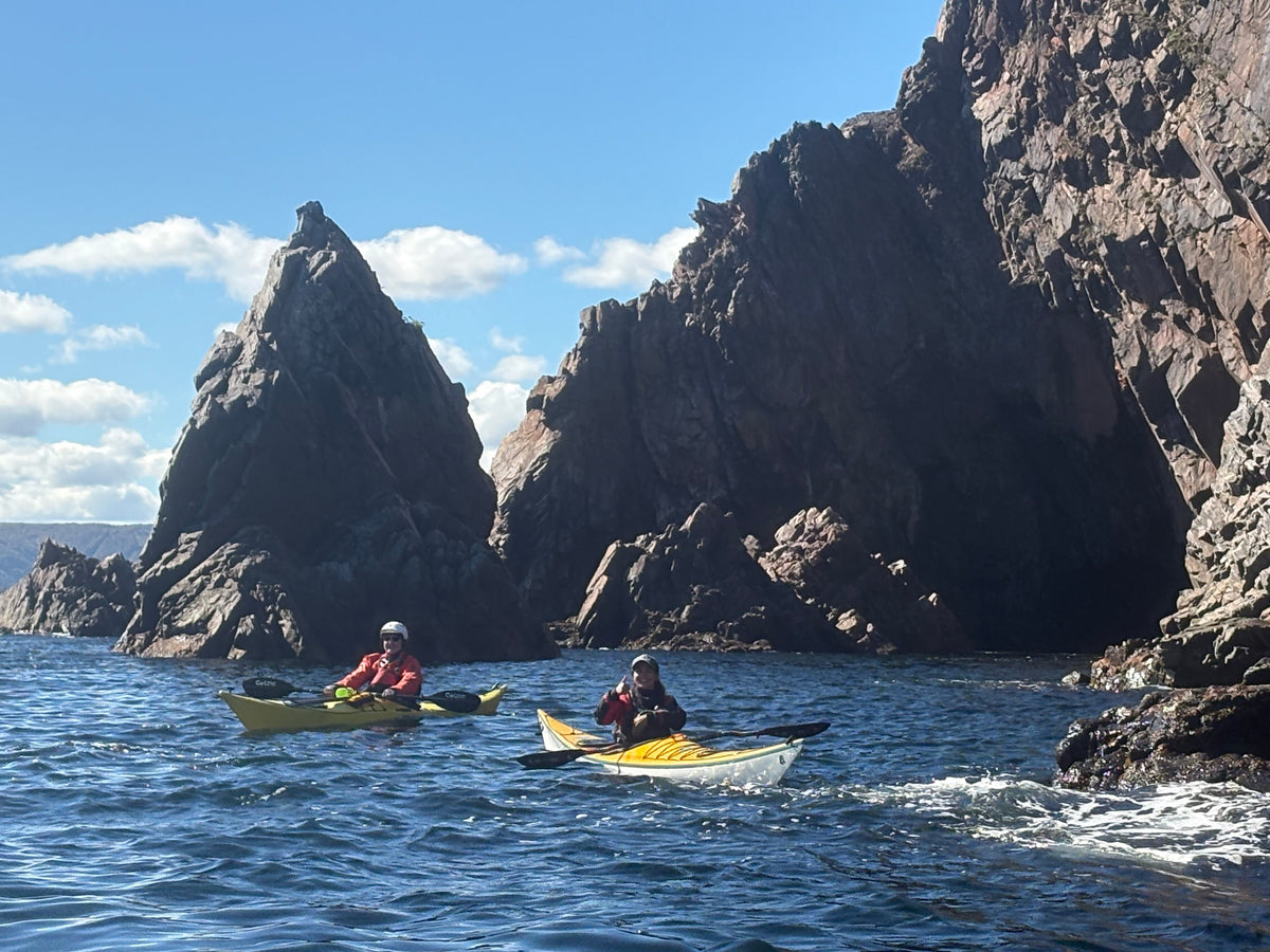 Two sea kayakers below tall dark cliffs off Ingonish Island, Cape Breton