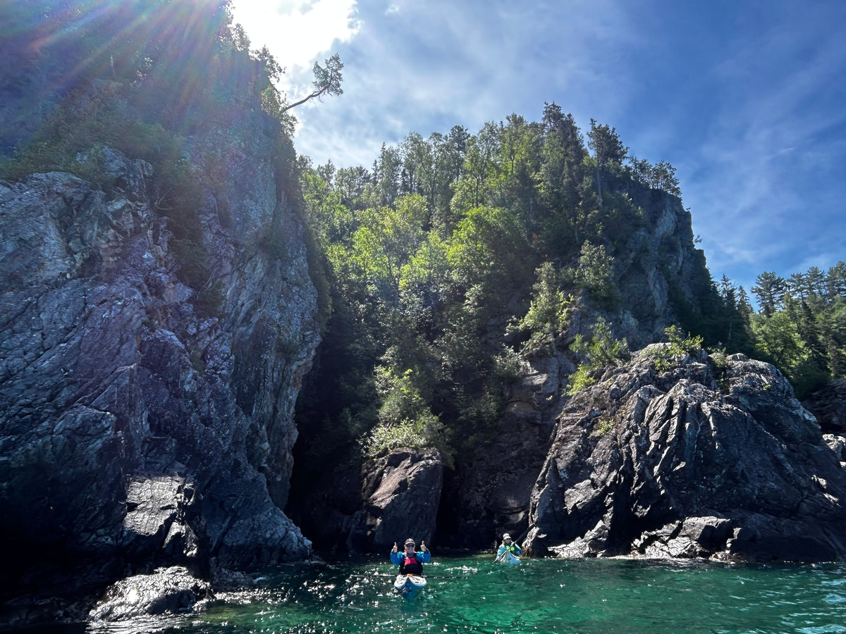 A sea kayaker below tall, tree-topped cliffs at Cap Chaillon, Lake Superior Provincial Park